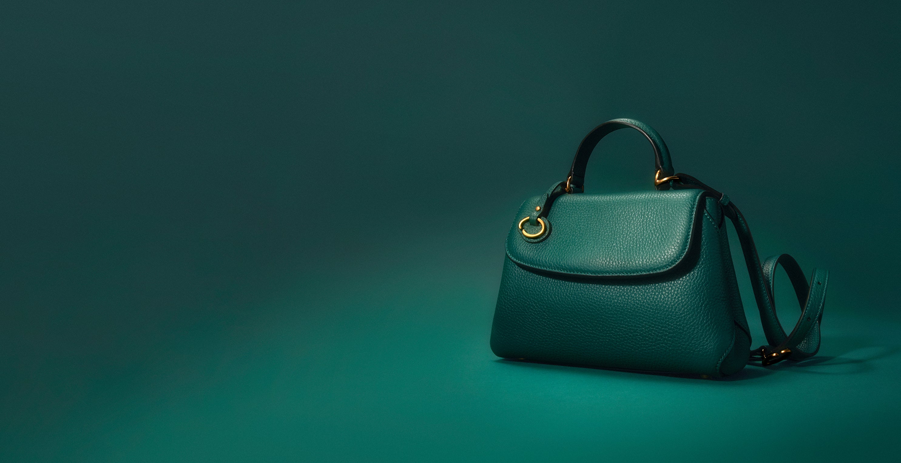 The homepage hero image features Oscar de la Renta's The Mini Poppy in Juniper green from the designer's signature collection. The handbag features a top handle and crossbody straps. 