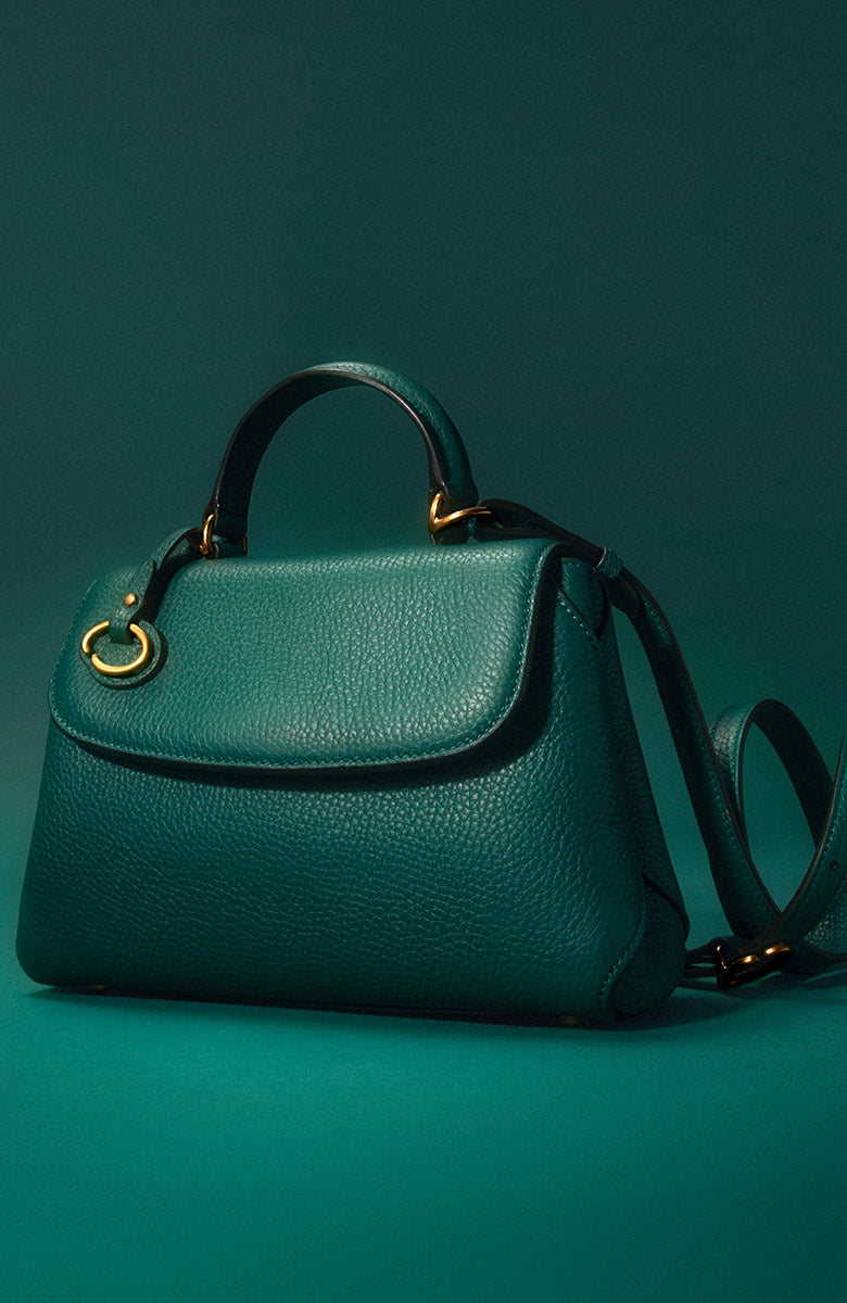 The homepage hero image features Oscar de la Renta's The Mini Poppy in Juniper green from the designer's signature collection. The handbag features a top handle and crossbody straps. 