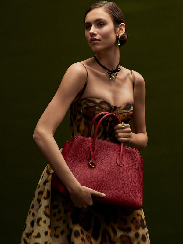 The model is wearing a cheetah print dress and carrying a maroon shoulder bag. She is wearing a black choker with a crystal heart pendant. 