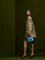 The model is wearing a cheetah print coat and matching skirt. She is holding a denim blue purse. 