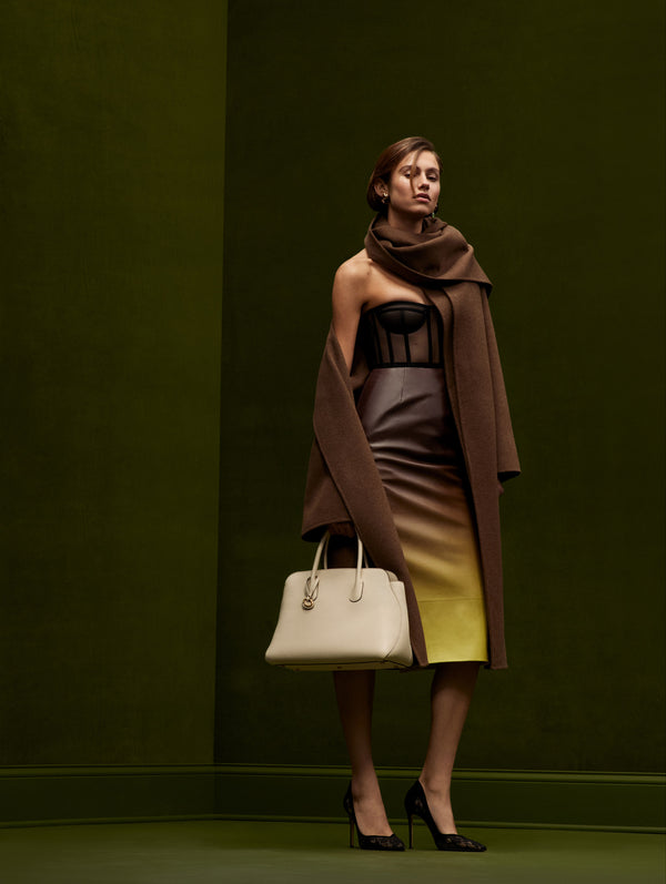 The model is wearing an ombre skirt and chocolate brown coat from Oscar de la Renta's Fall 2024 collection. 