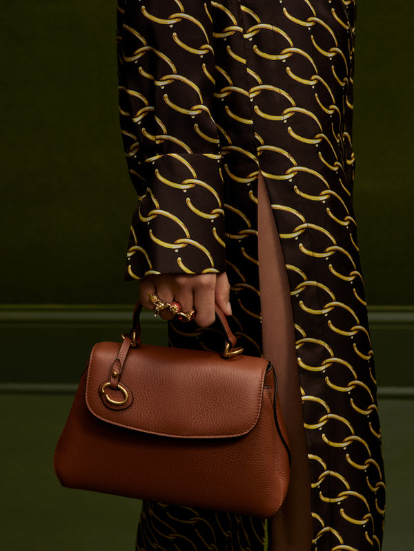 Close up of model holding the Poppy handbag in Brown while wearing an Oscar chain-link dress.