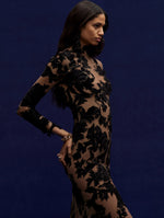 The model is wearing a black long dress in peony velvet guipure.