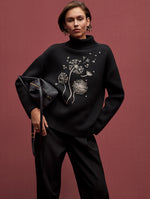 The model poses in a black turtleneck with a dandelion embroidered with crystals, aired with black pants and a black bag.