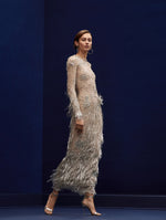 The model wears a crystal embellished long sleeve gown with fringe towards the bottom.