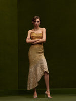 The model is wearing an ombre gold strapless embellished dress with an asymmetrical bottom