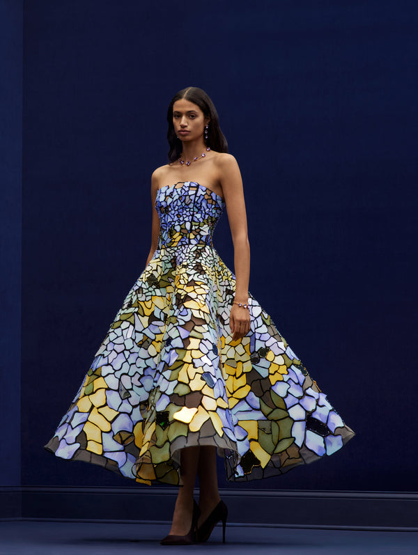 Model is wearing a strapless stain glass gown in blue and yellow.