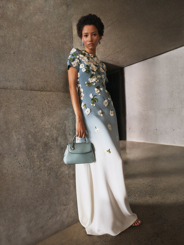 The model poses indoors in a Pre-Fall 2025 gown with a Oscar de la Renta signature handbag. 