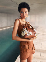 A model poses in front of an indoor pool in an Oscar de la Renta Pre-Fall 2025 knit mini dress and signature duffle handbag.