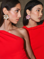 Two models pose in Pre-Fall 2025 looks from Oscar de la Renta’s latest collection. Both wear red gowns and flower earrings. 