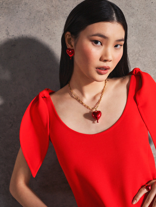 A model poses indoors in a red gown and matching heart shaped jewelry from Oscar de la Renta’s Pre-Fall 2025 collection.