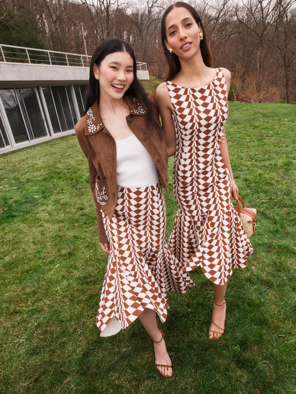 Two models pose in Pre-Fall 2025 looks from Oscar de la Renta’s latest collection. One model wears a midi dress in an abstract print, and the other wears a brown suede jacket and skirt in the same abstract print. 