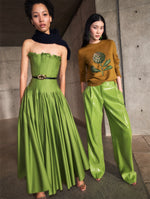 Two models pose in Pre-Fall 2025 looks from Oscar de la Renta’s latest collection. One model wears a green cotton poplin strapless maxi dress, and the other wears a knit pullover and green sequin pants.  