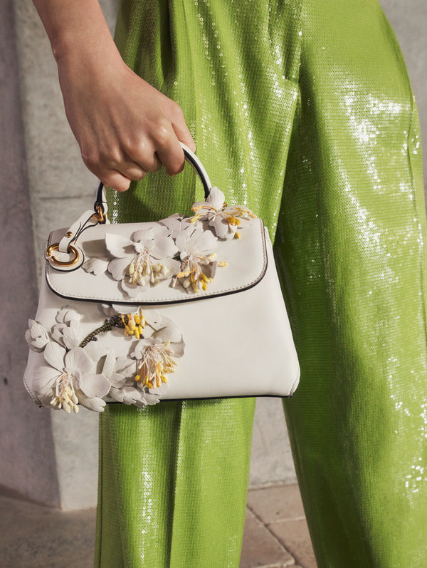 A model poses indoors in green sequin pants, paired with an embroidered white handbag, from Oscar de la Renta’s Pre-Fall 2025 collection. 