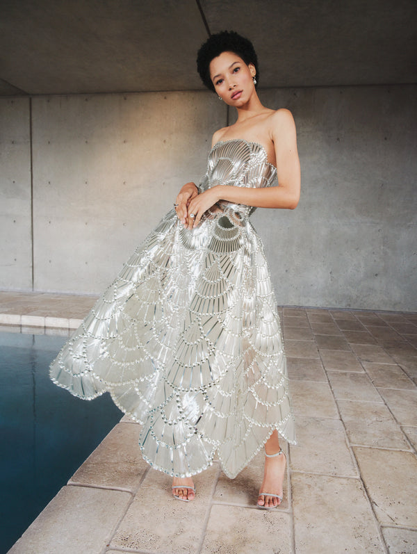 A model poses indoors in a silver embroidered cocktail dress from Oscar de la Renta’s Pre-Fall 2025 collection. 