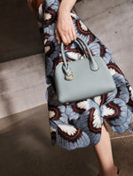 A model poses indoors with an Oscar de la Renta blue signature handbag from their Pre-Fall 2025 collection. 