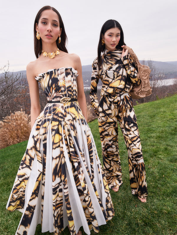 Two models pose in Pre-Fall 2025 looks from Oscar de la Renta’s latest collection. One model wears a butterfly printed cotton poplin strapless maxi dress, and the other model wears a butterfly printed blouse and pant set. 