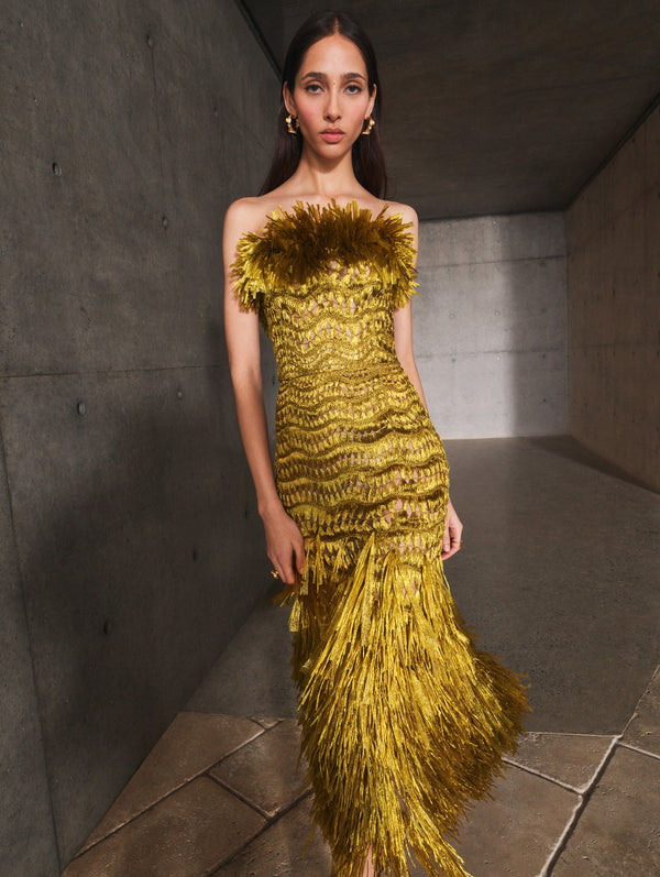 A model poses indoors in a gold strapless raffia fringe gown from Oscar de la Renta’s Pre-Fall 2025 collection. 