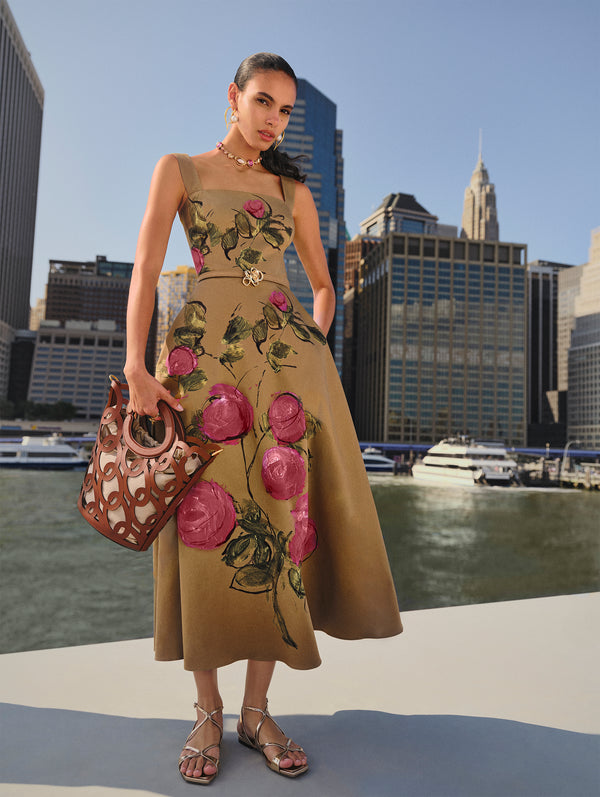 The model poses in a tan dress with a pink abstract, hand-painted iteration of the #odlrspring2025 rose by Co-Creative Director Fernando Garcia against the New York City skyline. 