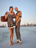 Two models pose against the New York City skyline. The model on the left is in a brown and black geometric minidress and the model on the right is in matching geometric brown and black pants and a brown polo knit sweater from Oscar de la Renta's Spring 2025 collection. 