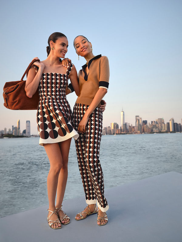 Two models pose against the New York City skyline. The model on the left is in a brown and black geometric minidress and the model on the right is in matching geometric brown and black pants and a brown polo knit sweater from Oscar de la Renta's Spring 2025 collection. 