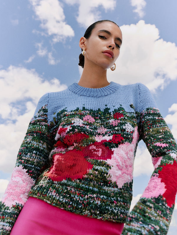 The model is wearing a knit pullover sweater depicting pink and red English roses against the blue sky. 