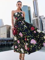 The model is wearing a strapless fit and flare black dress adorned with pink, red and white English roses. 