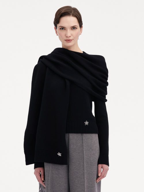 Model wearing the O Flower Cashmere Scarf in black, with a black cashmere sweater under, paired with grey trousers. Front View