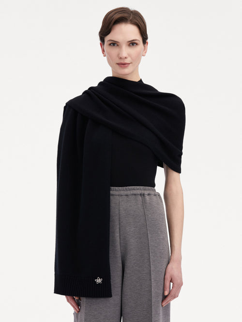 Model wearing the O Flower Cashmere Scarf in black, with a black cashmere sweater under, paired with grey trousers. Front View