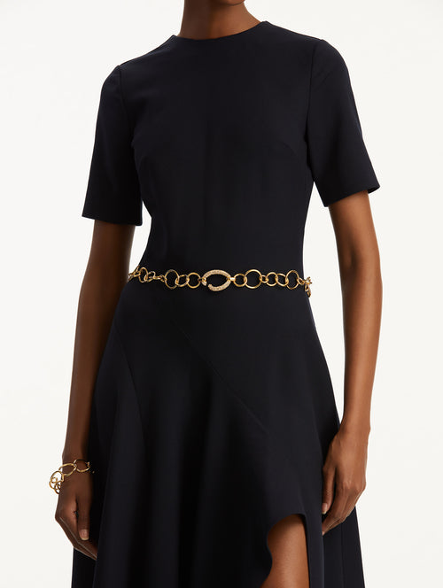 The model is wearing a navy short sleeve dress with a Pavé O Gold Chain-Link belt.