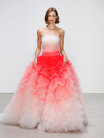 The model walks the runway in an ombré tulle tiered evening gown where shades of white transition to bright orange to white again.